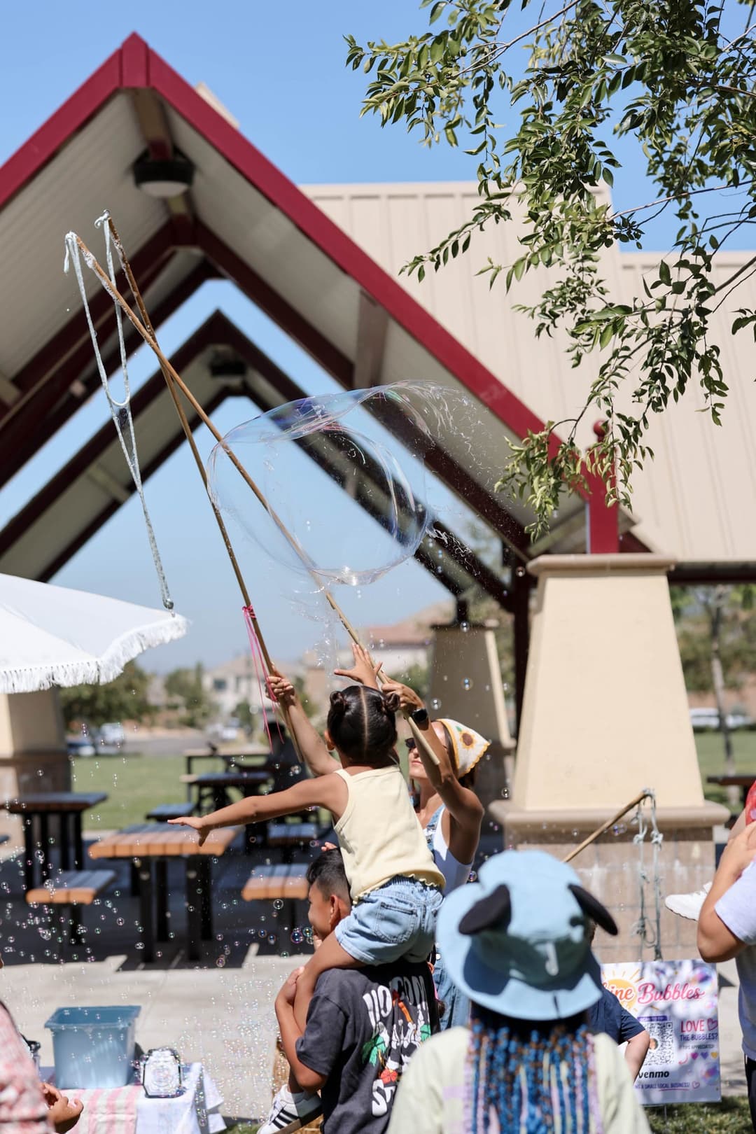 Child on shoulders reaching for a giant bubble